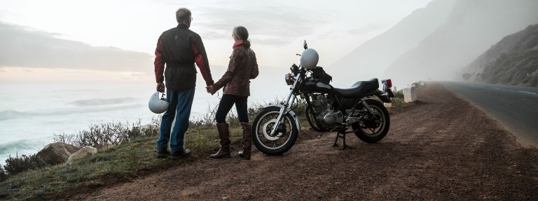 Mann und Frau stehen vor ihrem Motorrad und blicken von einem Berg herab