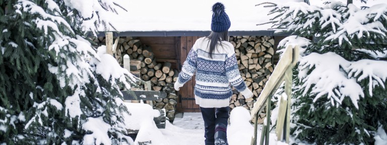 Frau läuft schneebedeckte Treppe zu einem schneebedeckten Holzhaus hinunter