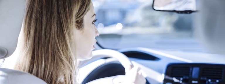 Junge Frau blickt konzentriert durch Frontscheibe eines Autos