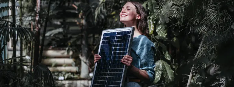 Frau hält ein Solarmodul mit geschlossenen Augen in die Sonne