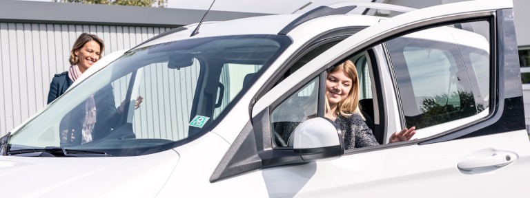 Junge Frau steigt lächelnd aus weißem Auto aus