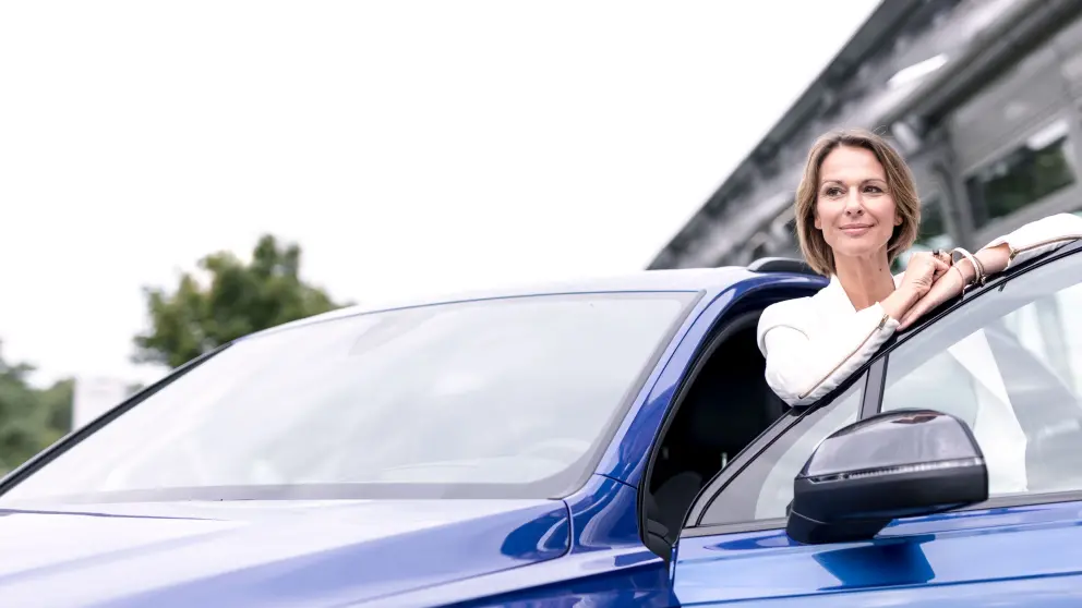 Frau mittleren Alters steht vor blauem Auto