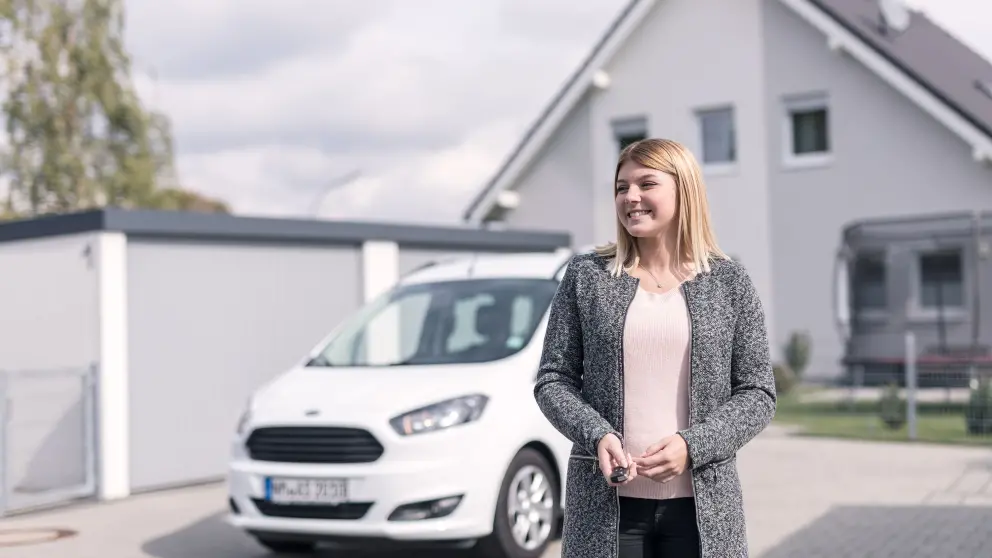 Junge Frau steht vor weißem Auto und lacht