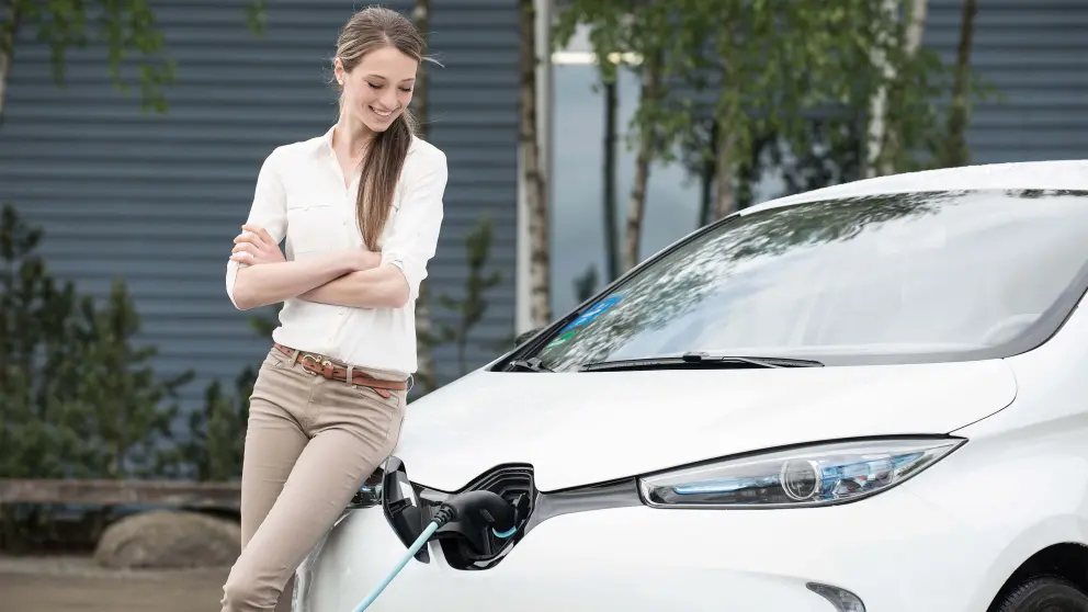 Junge Frau lehnt an einem weißen Elektroauto