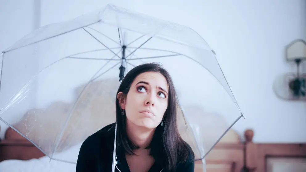 Junge Frau sitzt in Wohnung unter einem Regenschirm