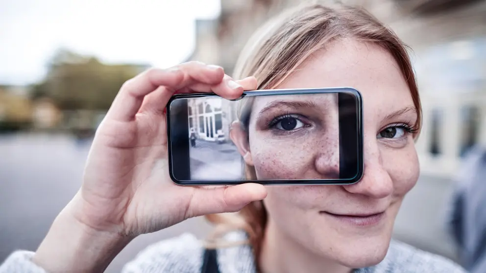 Frau hält sich Smartphone vor ihr Auge, welches wiederum auf dem Smartphone zu sehen ist