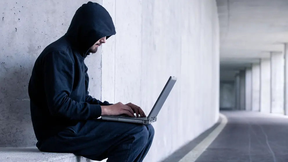 Mann in dunklem Kapuzen-Pullover arbeitet an einem Laptop auf seinem Schoß