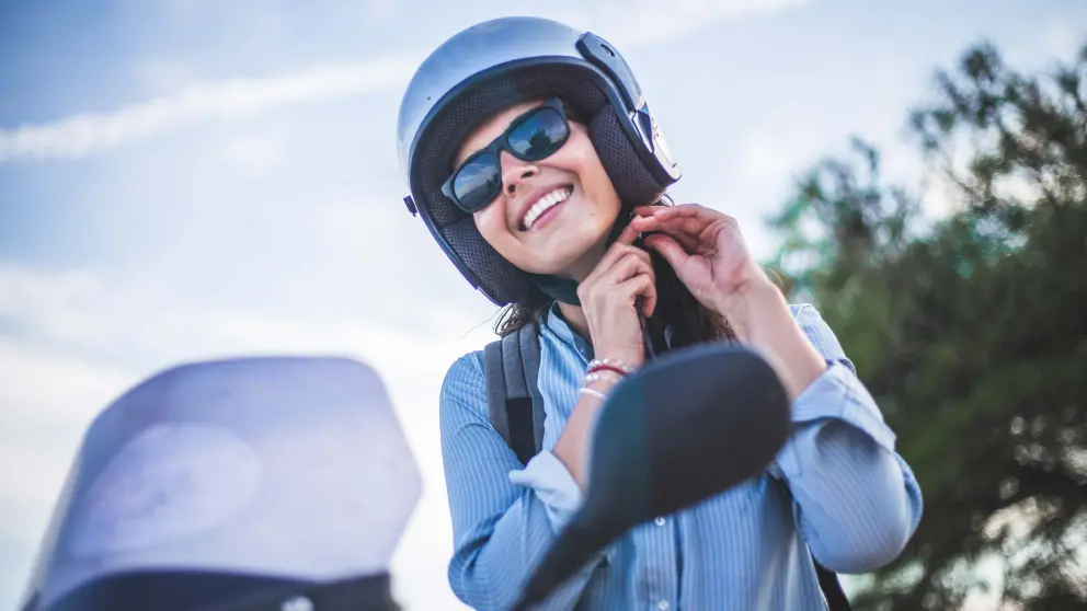 Frau mit Sonnenbrille schließt ihren Helm und sitzt auf einem Roller