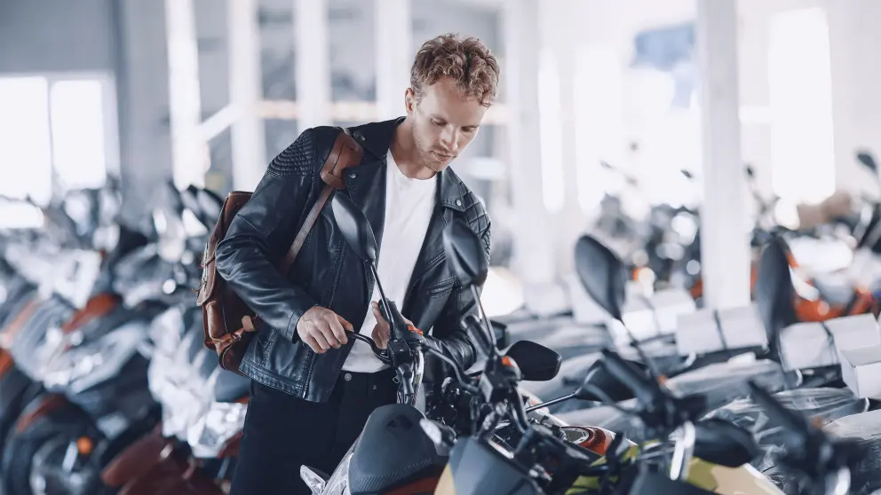 Junger Mann in schwarzer Lederjacke schaut sich Motorrad in einem Geschäft an