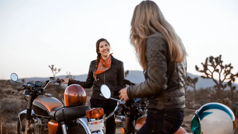 2 Frauen in Lederjacke lachen sich neben ihren Motorrädern an