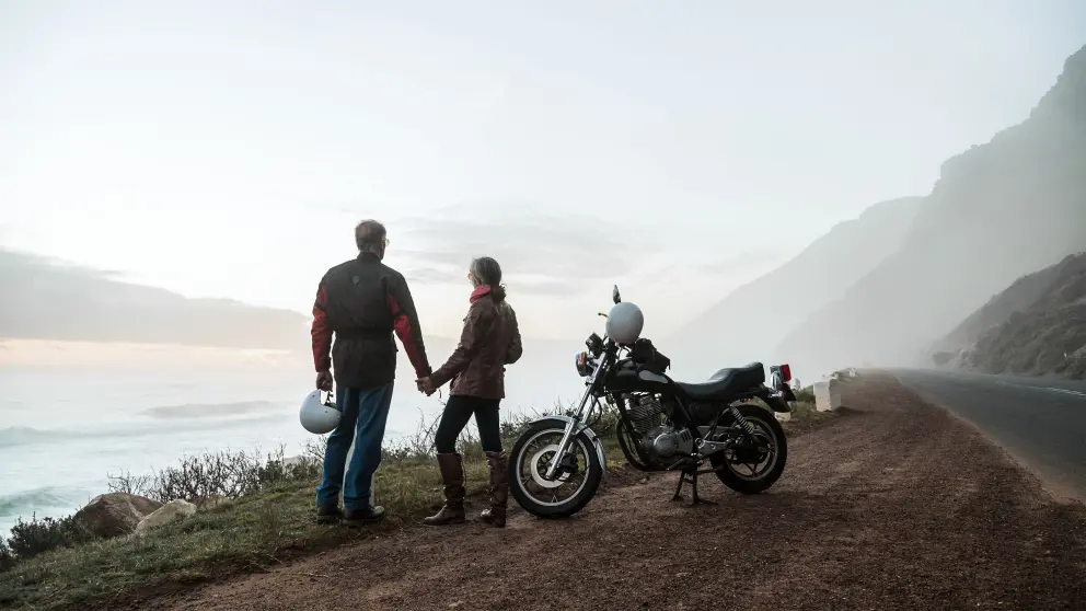 Mann und Frau stehen vor ihrem Motorrad und blicken von einem Berg herab