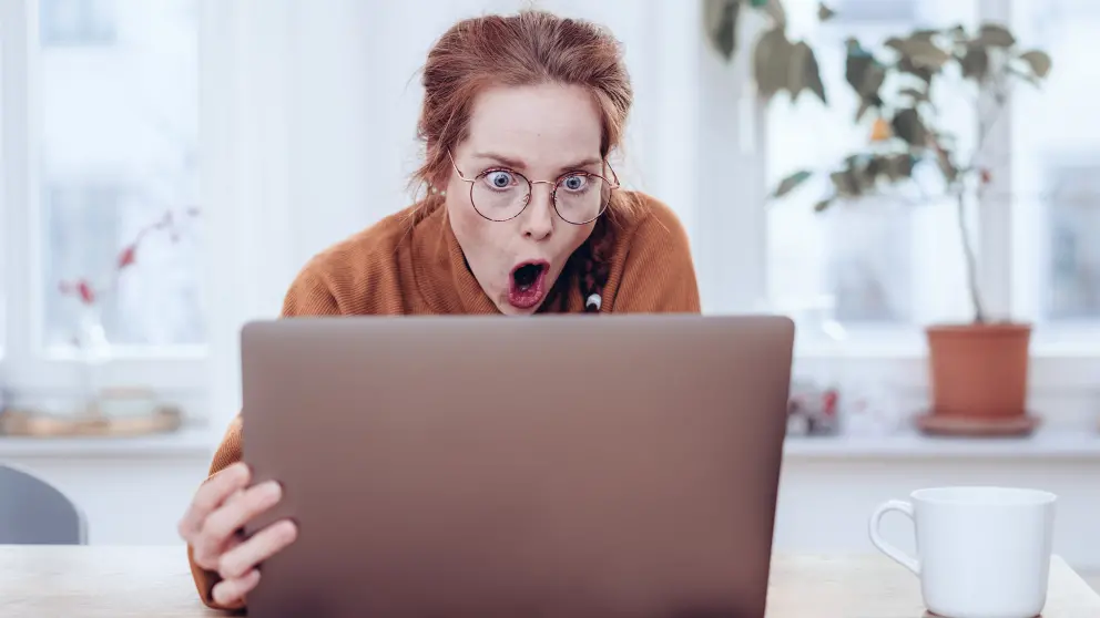 Frau sitzt vor einem Laptop und reißt ihren Mund und ihre Augen weit auf