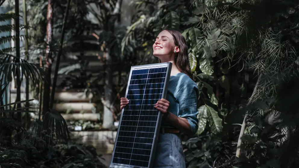 Frau hält ein Solarmodul mit geschlossenen Augen in die Sonne