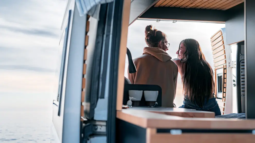 Junges Paar blickt aus einem Wohnmobil aufs Meer