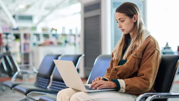 Eine Frau sitzt mit einem Laptop im Wartebereich am Flughafen