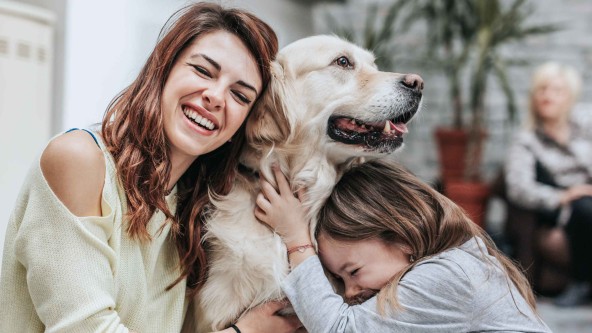Frau und Mädchen drücken sich lachend an einen Hund