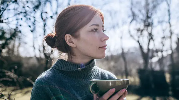 Rothaarige Frau steht im Garten mit einer Tasse in der Hand