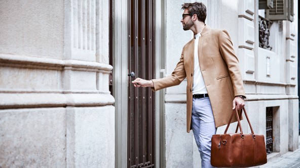 Mann mit großer brauner Tasche sperrt Haustür auf