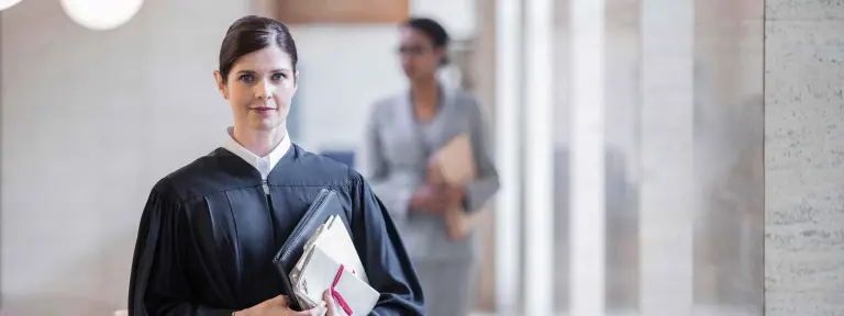 Anwältin ist in ihrer Robe gekleidet und hält in einem großen hellen Gebäude einen gebundenen Papierordner in den Händen