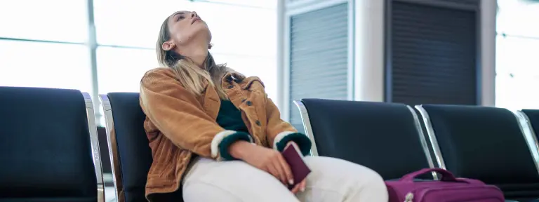 Eine Frau sitzt entnervt in einem Wartebereich am Flughafen