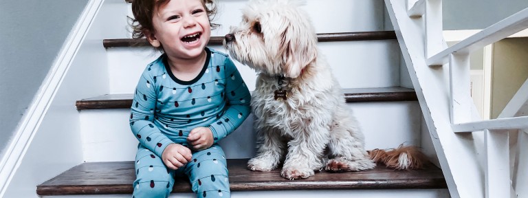 Kind sitzt lachend mit Hund auf Treppe