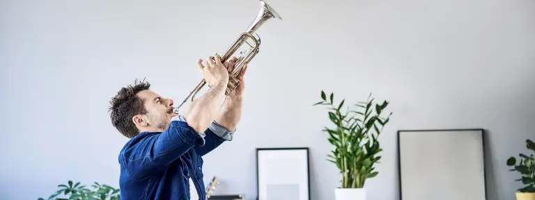 Mann spielt in seiner Wohnung Trompete