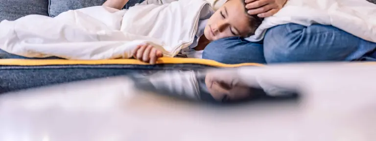 Mutter liegt mit schlafendem Sohn auf der Couch und streichelt seinen Kopf