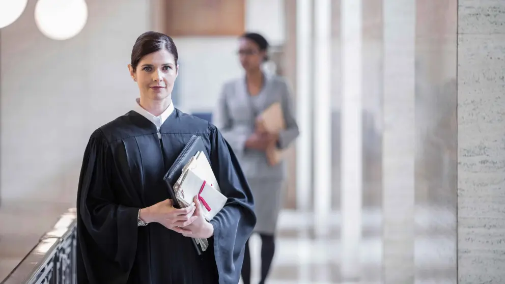Anwältin ist in ihrer Robe gekleidet und hält in einem großen hellen Gebäude einen gebundenen Papierordner in den Händen