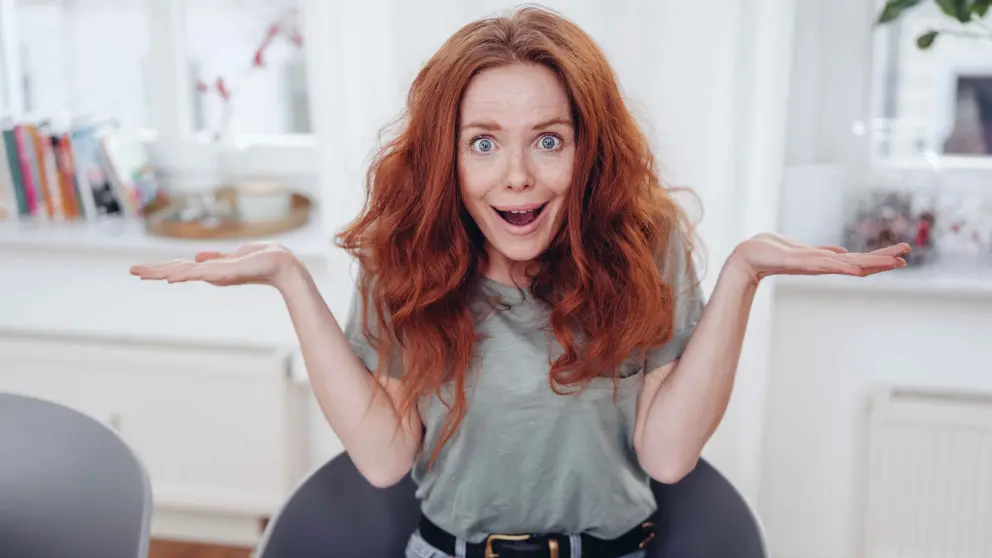 Eine junge Frau mit langen roten Haaren sitzt ratlos auf einer Couch