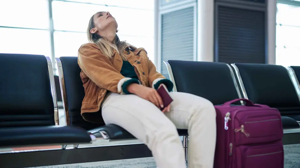 Eine Frau sitzt entnervt in einem Wartebereich am Flughafen