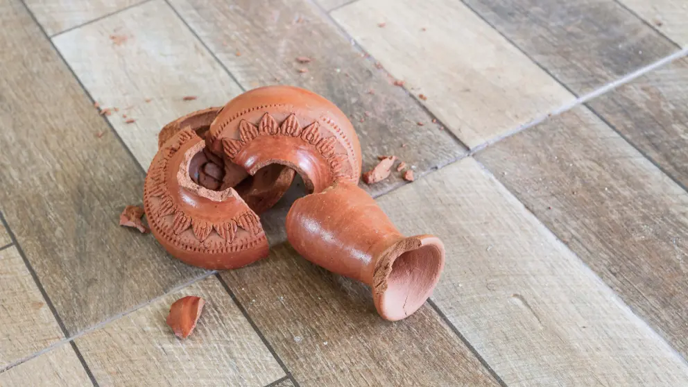 Zerbrochene braune Vase liegt auf einem Holzboden