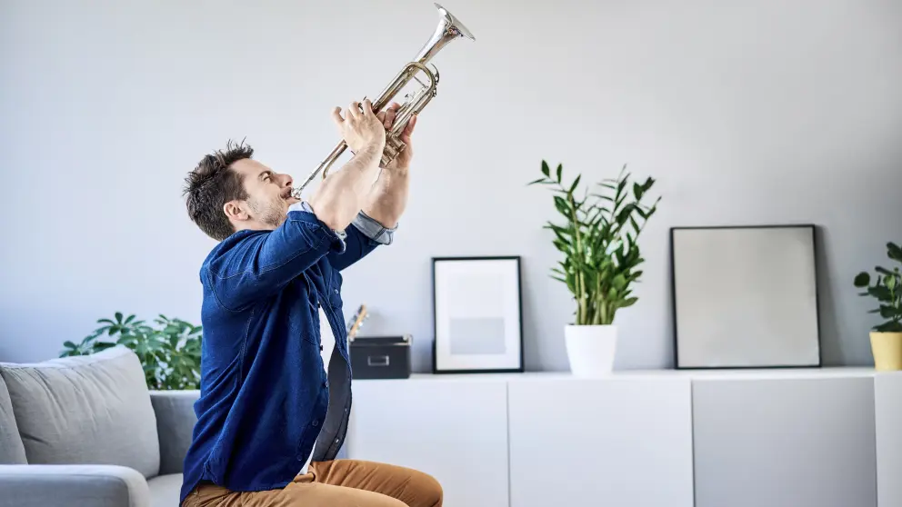 Mann spielt in seiner Wohnung Trompete