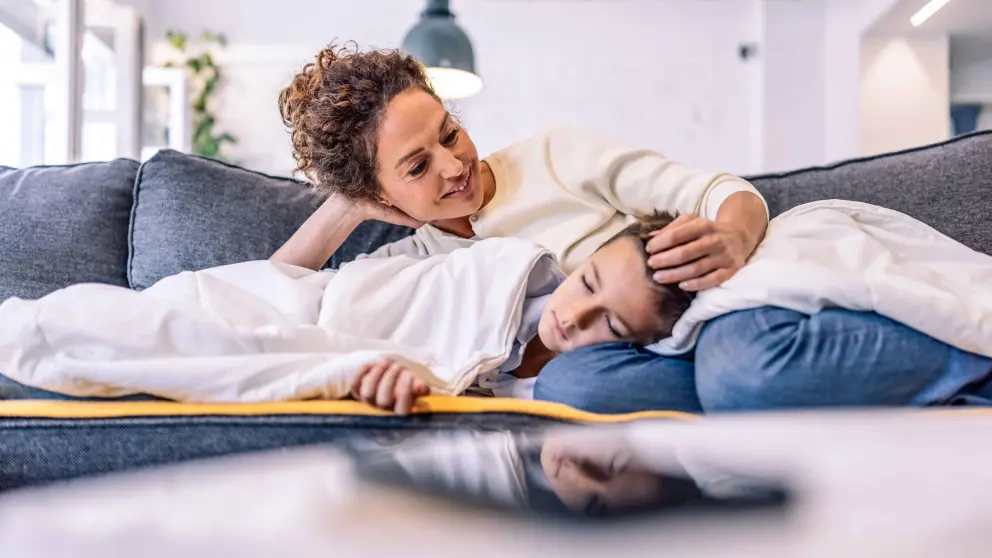 Mutter liegt mit schlafendem Sohn auf der Couch und streichelt seinen Kopf